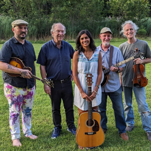 Five performers posing with their instruments outside in a grassy area.